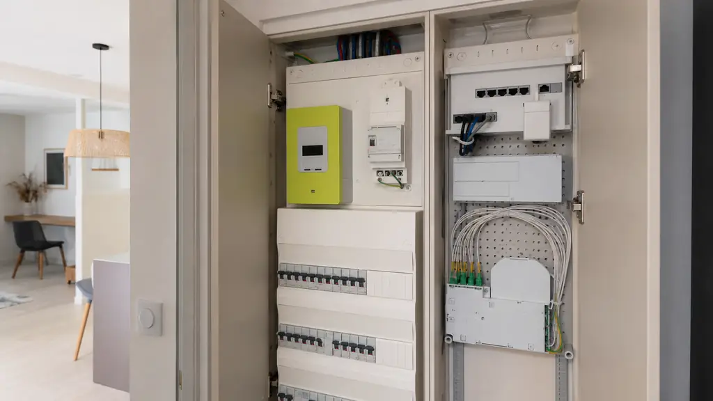 Editorial photograph of an open residential GTL showing a Linky meter and branch circuit breaker above a distribution board, with a separate communication cabinet containing RJ45 ports and a fiber optic termination, no visible text or logos