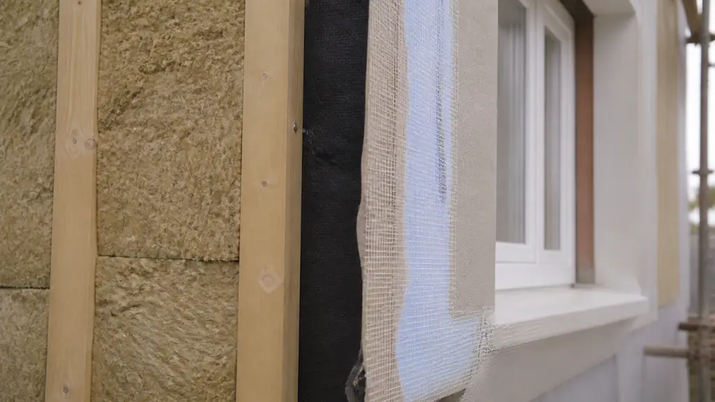 Close-up editorial photograph of a facade renovation in Saint-Jory, showing mineral wool fitted into a timber frame beside a ventilated air gap and an adjacent window surround prepared with reinforced mesh, no text, no logo